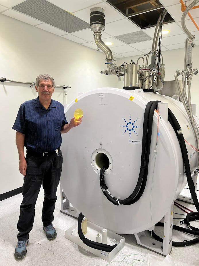 Stephen Russek poses in the lab holding a small model of a human head and standing next to the large cylinder of an MRI machine.